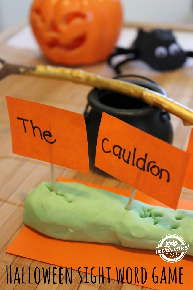 Halloween sight word game with orange sight word cards sticking out of green playdough with a mini black cauldron behind it.